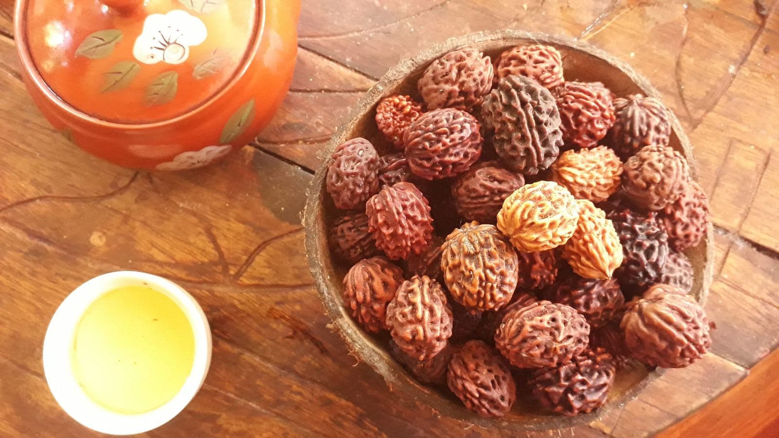 Rudraksha beads resting in a carved wooden bowl beside a dish of oil